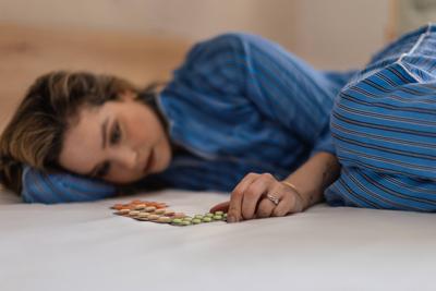 Young woman with depression lying in bed, looking at pills. Young woman with depression lying in bed, looking at the pil-stock-foto