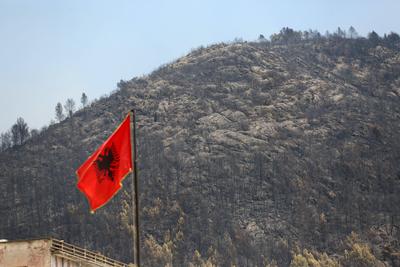 An Albanian flag is seen near a burned area near the town of Delvine, south-east Albania, on August 13, 2025, as fire cr-stock-foto