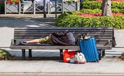 Ein Obdachloser liegt auf einer Bank und schl?ft. Sein Hab und Gut steht bei ihm. (Freiburg im Breisgau, Deutschland, 0-stock-foto