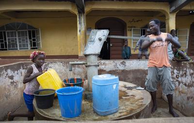 Bomeh Village auf der KissyRoad Muellkippe. Maedchen und Mann an der Wasserpumpe, die nur giftiges Wasser liefert, Freet-stock-foto