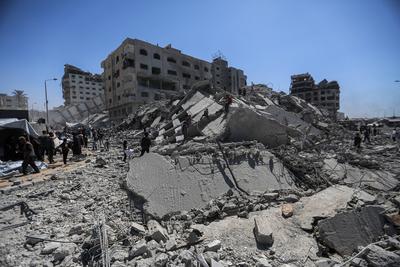 Palestinians walk through the rubble of the Tiba tower which crashed to the ground moments after Israeli strikes-stock-foto