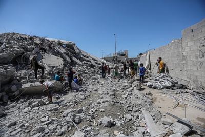 Palestinians walk through the rubble of the Tiba tower which crashed to the ground moments after Israeli strikes-stock-foto
