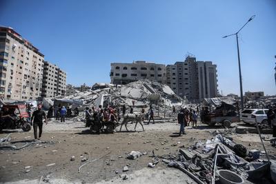 Palestinians walk through the rubble of the Tiba tower which crashed to the ground moments after Israeli strikes-stock-foto