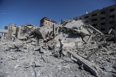Palestinians walk through the rubble of the Tiba tower which crashed to the ground moments after Israeli strikes-stock-foto