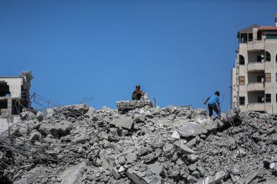 Palestinians walk through the rubble of the Tiba tower which crashed to the ground moments after Israeli strikes-stock-foto