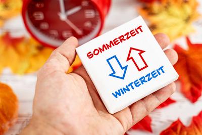 9 October 2023: Daylight saving time and winter time with two arrows on a board in one hand. Symbol image time change in-stock-foto