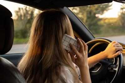 Happy young woman speaking by mobile phone while driving car. Business woman talking phone call in automobile. Unsafely-stock-foto