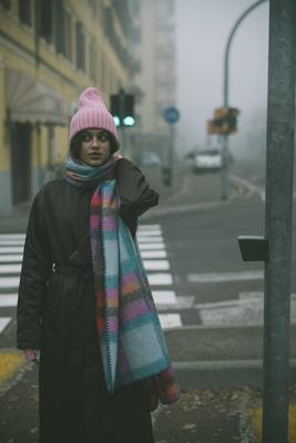 A woman in a pink hat and scarf stands on a foggy street-stock-foto