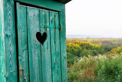 Heart shape on the old wooden toilet door, green toilet in the field. Outdoor recreation. Close-up. Heart shape on the o-stock-foto