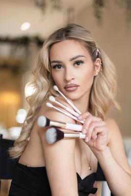 Mode sch?ne sexy Make-up-K?nstler glamour?se Frau Modell in modischen schwarzen Outfit mit tiefem Ausschnitt sitzt in Be-stock-foto