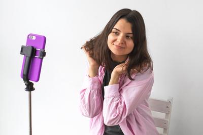 Junge Frau in rosa Hemd posiert f?r Selfie, Video-Aufnahme oder mit Video-Anruf mit Smartphone auf Stativ gegen wei?en Hintergrund, Konzept der sozialen Medien, Selbstdarstellung, Technologie-stock-foto