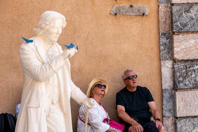 Taormina, Sizilien - Italien - 05-04-2025: Statue von Oscar Wilde mit blauen Schmetterlingen und zwei sitzenden Touristen an einer strukturierten Wand in Taormina, Sizilien, in der N?he einer Marmors?ule.-stock-foto