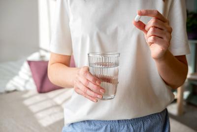 Nahaufnahme einer nicht erkennbaren Frau mit Tabletten und einem Glas Wasser in der Hand. Frau nimmt Medikamente ein. Behandlung Kurs oder Vitamine komplexe Idee. Gesundheitspflege Konzept.-stock-foto