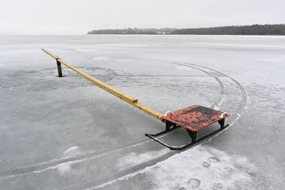 Frozen lake wih red sleigh and wtooden plank A desolate frozen lake with a solitary red sleigh attached to a long wooden-stock-foto