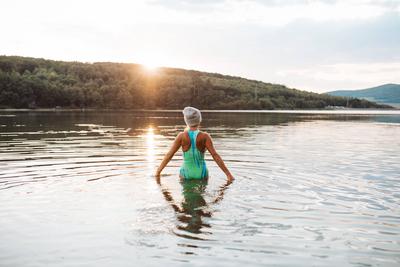 Cold water swimming for elderly women. Senior sporty women standing in lake during cold evening, looking at setting sun.-stock-foto