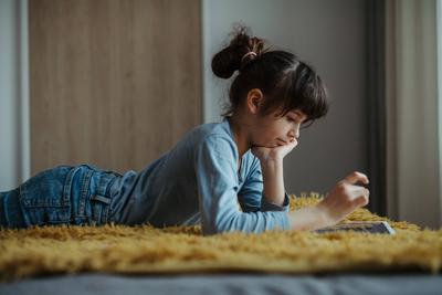 Cute girl lying on belly, scrolling on smartphone. Using social media. Side view. Cute girl lying on belly on the floor,-stock-foto
