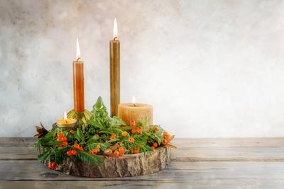 Vier Variationen von Kerzen mit naturgr?nen Zweigen und orangefarbenen Beeren auf einer Baumscheibe als Advents- und Weihnachtsdekoration, rustikale beige Hintergrundwand mit Kopierfl?ch-stock-foto