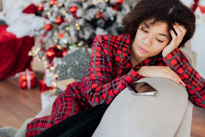 Junge Afrikanerin im Pyjama sitzt auf der Couch und schaut nachdenklich auf ihr Telefon. Das schwarze M?dchen ist traurig und wartet auf einen Anruf.-stock-foto