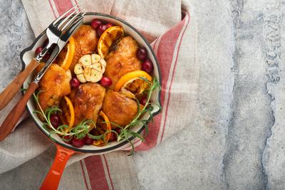 Gebackene H?hnchenschenkel mit Orange, Preiselbeeren und w?rzigen Kr?utern Rosmarin serviert in der Pfanne auf hellem Hintergrund. Festliches Weihnachtsessen Konzept Men?. Ansicht von oben. copy space-stock-foto