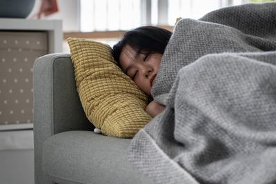 Kranke asiatische Frau, die zu Hause auf dem Sofa unter einer Decke schl?ft und sich von einer Grippe erholt-stock-foto