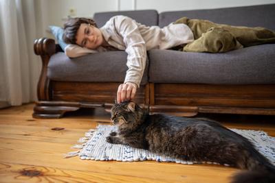 M?de Frau, die sich zu Hause ausruht und ihre Katze streichelt, die neben der Couch auf einem weichen Teppich liegt, langsames Leben-stock-foto