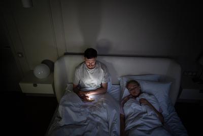 Ersch?pfter Mann wacht allein im Bett und scrollt aufgrund von Schlaflosigkeit und digitaler Sucht zu sp?ter Stunde auf seinem Handy-stock-foto