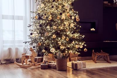 Christmas decor in cosy, domestic living room with christmas tree with lighting strings, balls, wooden rocking chair, gifts wrapped in craft paper, sledge. Background with copy space-stock-foto