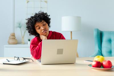 Schl?frige traurige afroamerikanische Frau sitzt am Tisch mit Laptop. M?de ?berarbeitetes M?dchen faul zu arbeiten. Student Gesch?ftsfrau entspannend gelangweilt im B?ro zu Hause nach der Arbeit am Laptop-Computer.-stock-foto