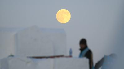 HARBIN, CHINA - DECEMBER 04: A full moon lights up the sky with a worker braves cold to build snow sculpture at the cons-stock-foto