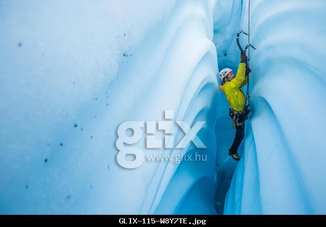 Man in yellow coat ice climbing a narrow and vertical canyon cut from solid glacier ice.