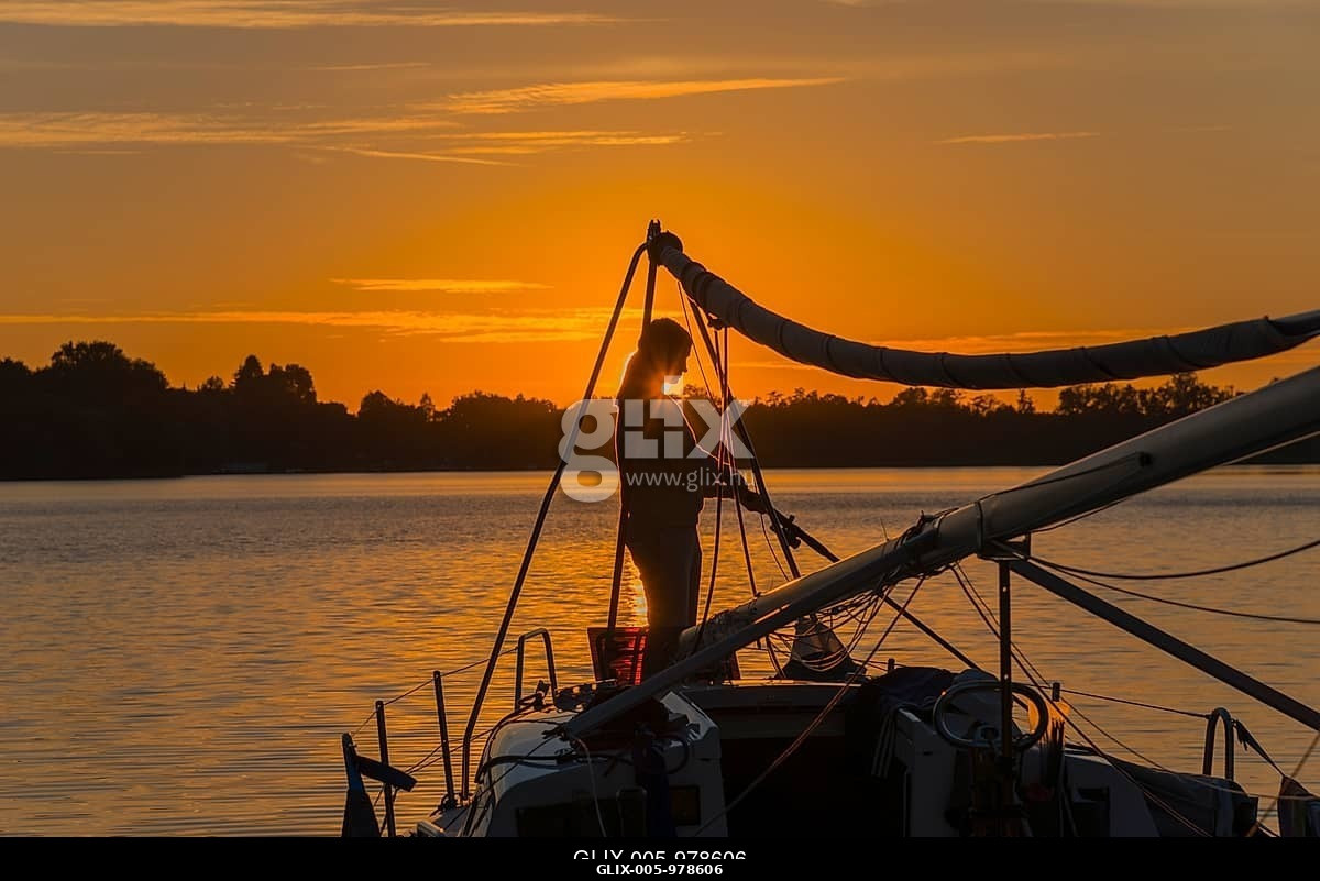 Silhouette of a woman on a sailing boat at sunset with orange sky, Lake Ilinsk, Jelonek, Milomlyn, Liebemühl, Ostródzki, Warmia-Masuria, Poland