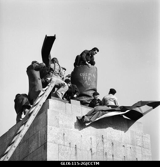 BUDAPEST 1956 Egy magyar zászló, középen a szovjet címer nélkül, egy szovjet katonát ábrázoló óriási szobor talapzatán, amelyet a felkelők ledönten...