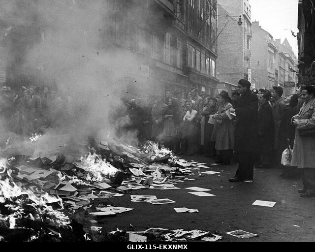 Egy magyar tömeg nézi, ahogy egy kifosztott orosz könyvesboltból származó könyveket és röpiratokat égetnek el egy budapesti utcában. 1956 október v...